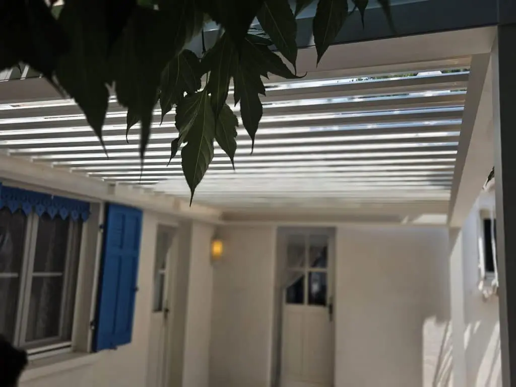Gestion optimale de la luminosité et de l'ombre sous le toit d'une pergola bioclimatique blanche adossée